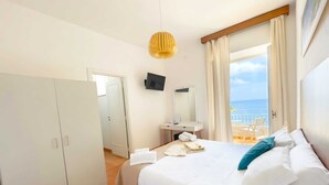 Une chambre d’hôtel avec un lit, un bureau, une télévision et une vue sur la mer.