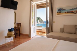 Une chambre à coucher comprenant un lit, une chaise, un téléviseur, un tableau et un balcon avec vue sur la mer.