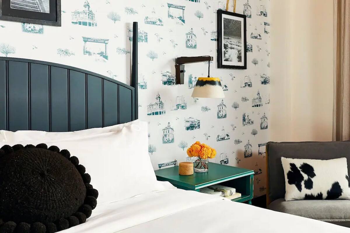A hotel room with a bed, a nightstand, a lamp, a chair, and a window with curtains.