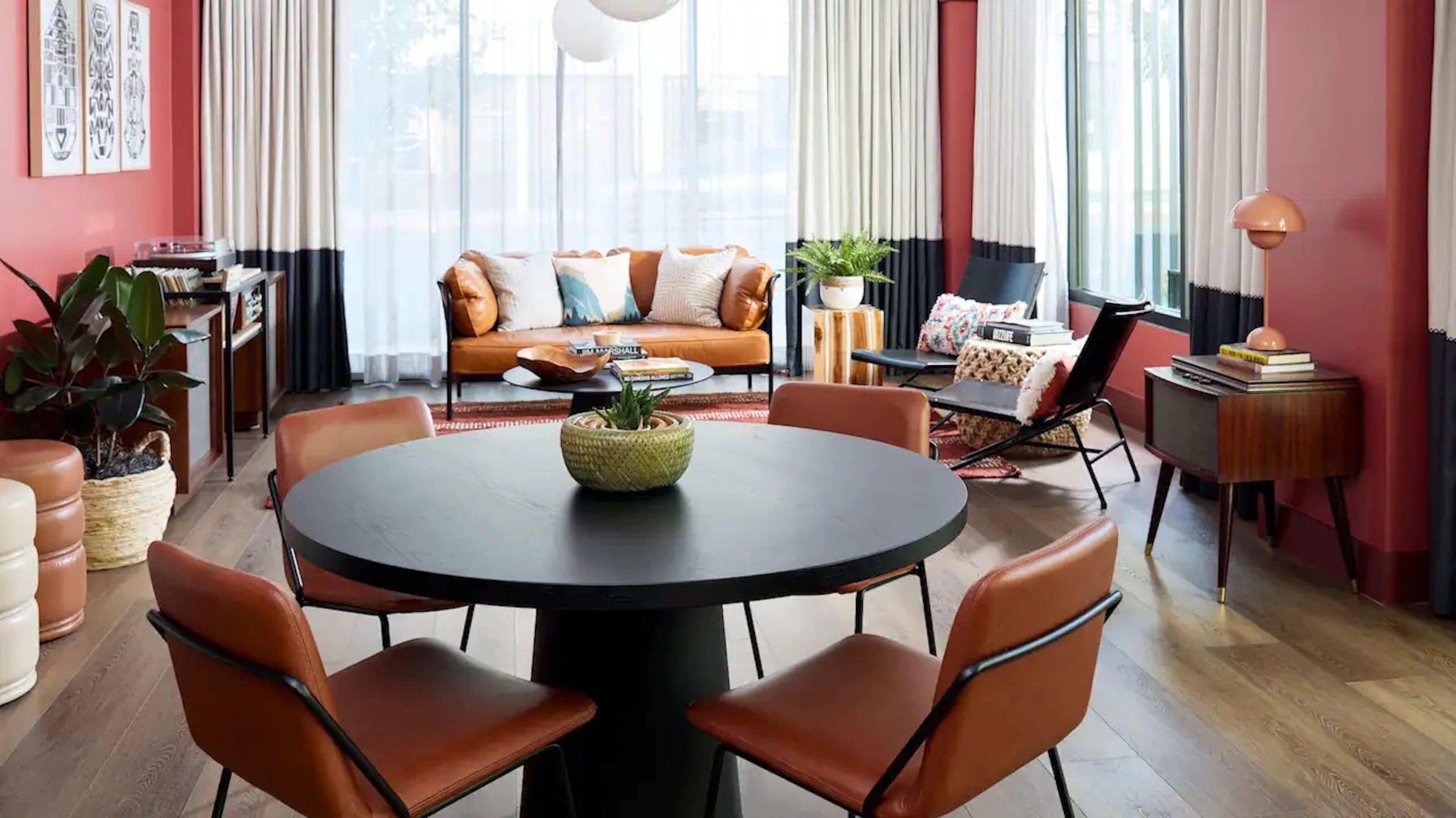A modern living room with a round table, leather chairs, a sofa with cushions, a coffee table, and a bookshelf.