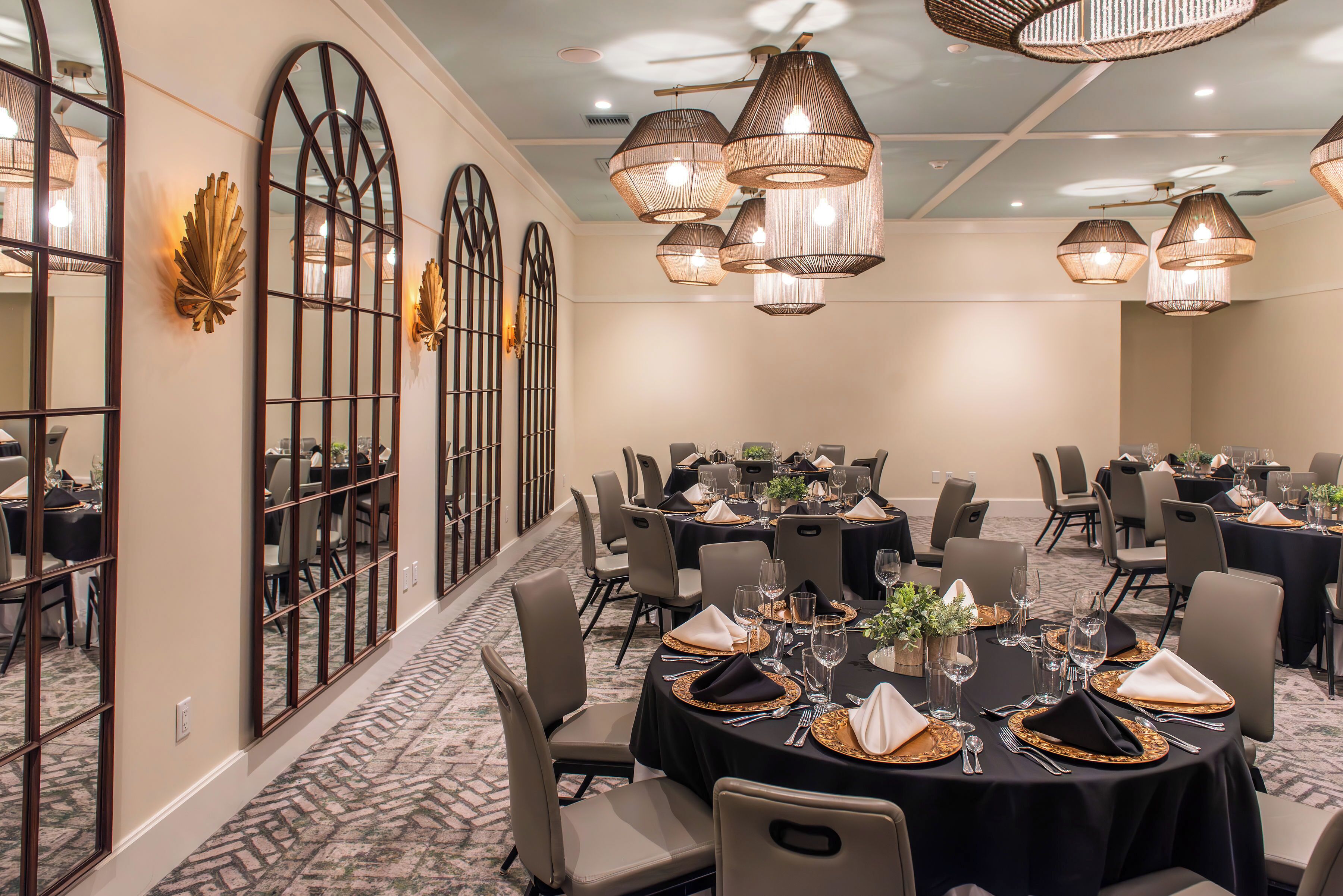 Un salón de banquetes con mesas redondas dispuestas para comer, grandes espejos en las paredes y múltiples lámparas colgantes.