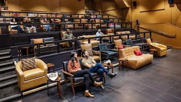 A spacious indoor seating area with tiered rows of chairs and couches, a staircase, and a stage.
