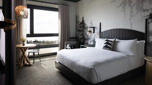 A modern hotel room with a large bed, a small table, a chair, and a view of the outdoors. - El Capitan Hotel (Merced)