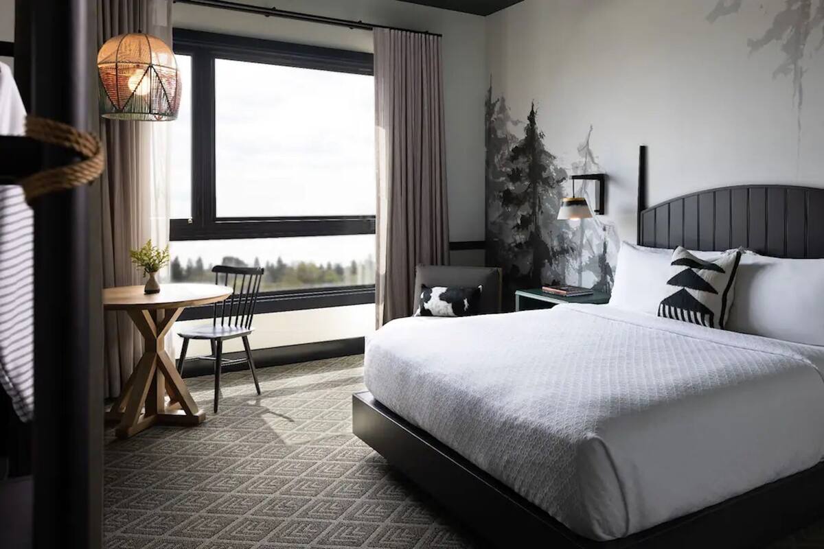 A modern hotel room with a large bed, a small table, a chair, and a view of the outdoors.