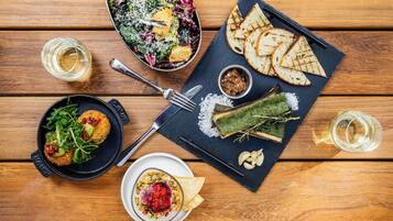 A wooden table with a variety of dishes including a salad, grilled bread, and a bowl of soup.