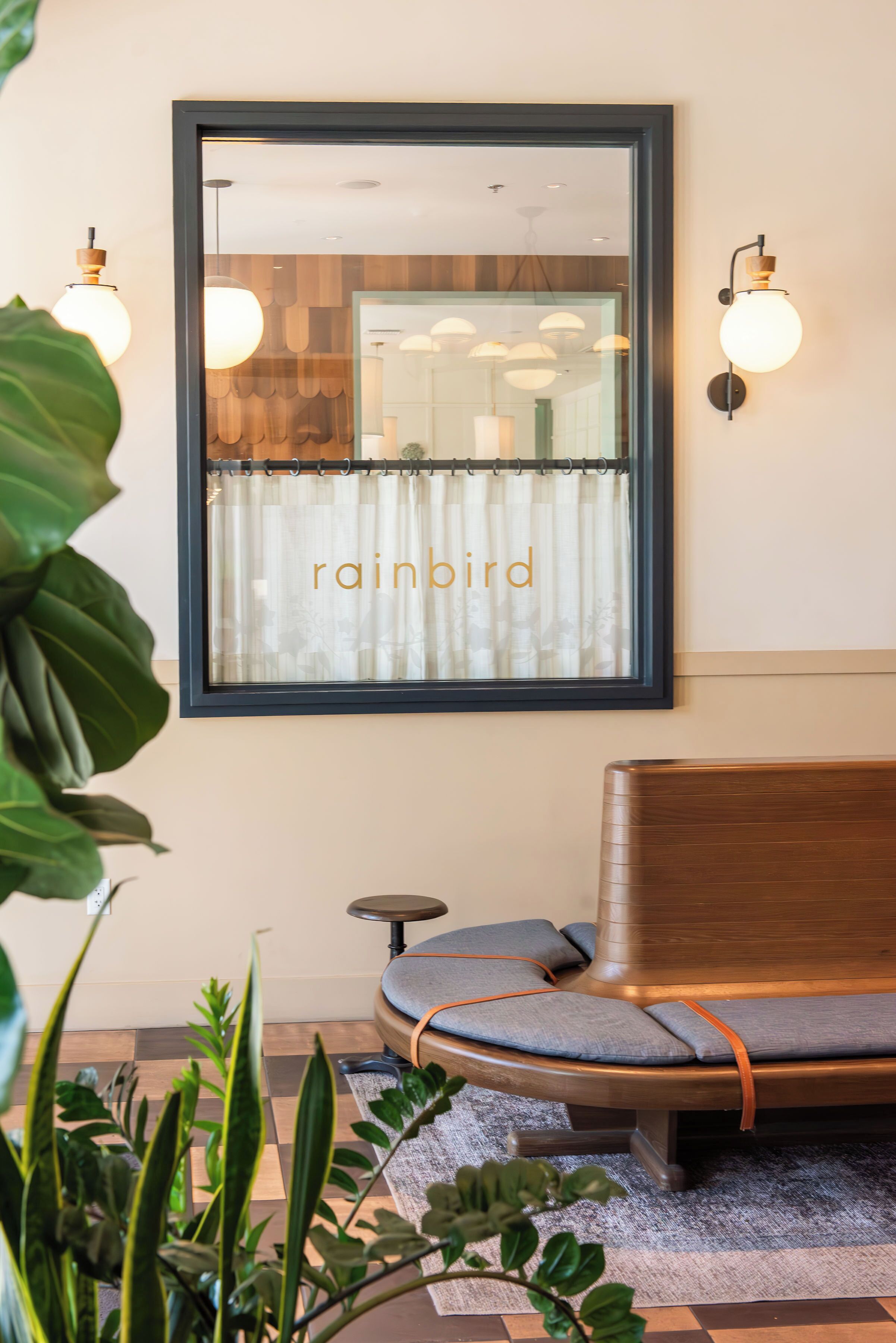 A modern waiting area with a large mirror, a wooden bench, and two wall-mounted lamps.