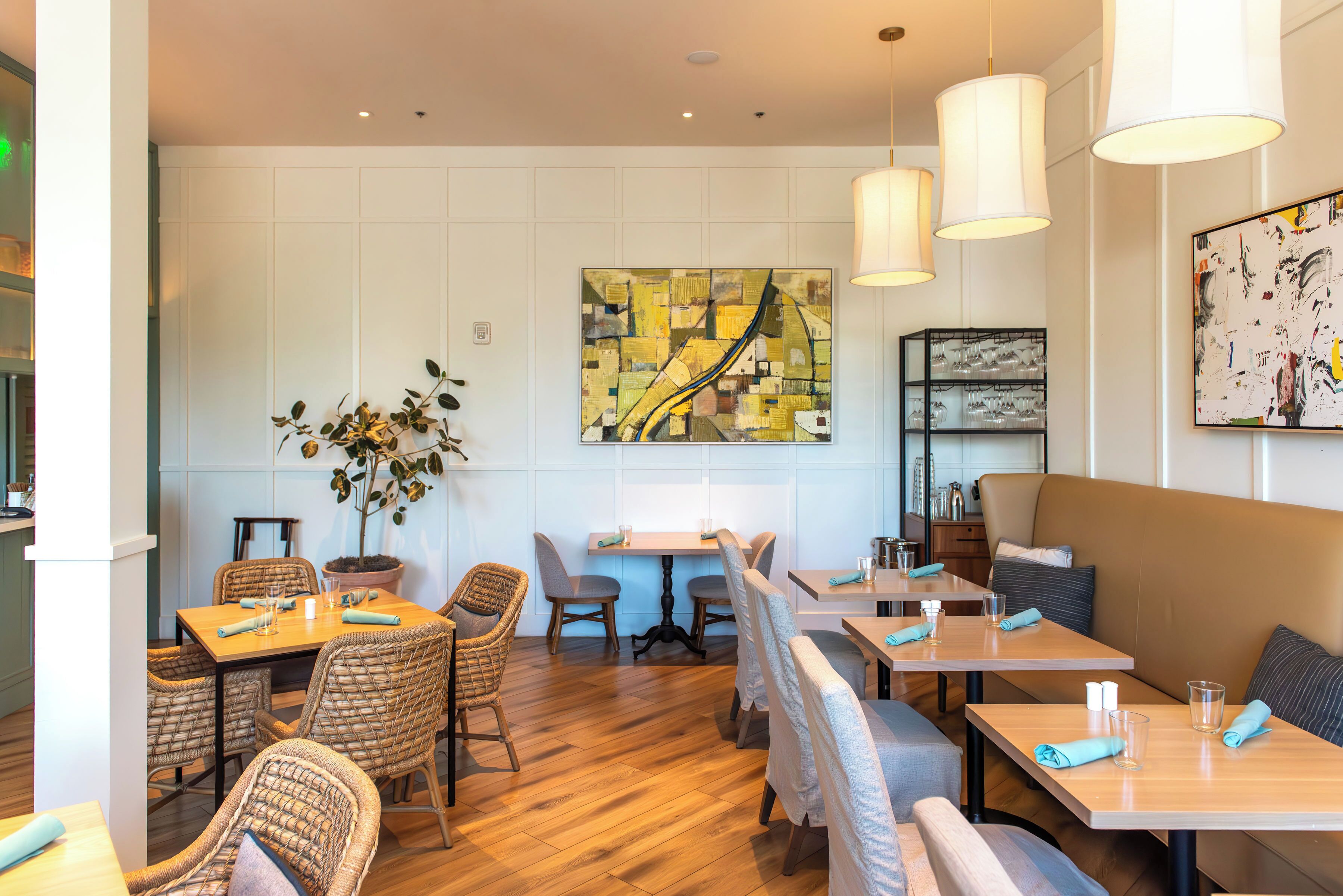 Un restaurante con mesas y sillas de madera, un cuadro grande en la pared y una planta en maceta.