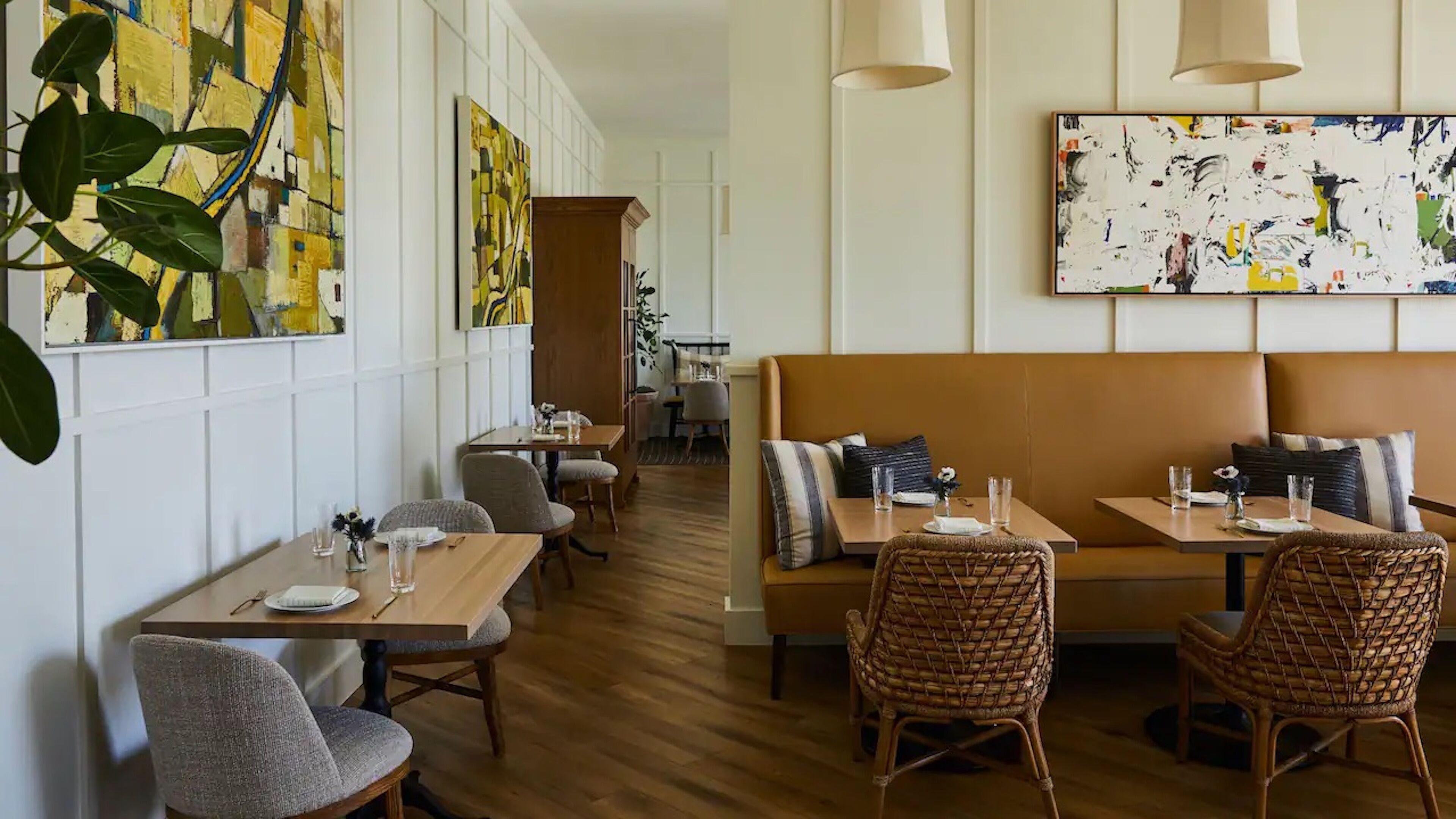 Un restaurant avec des tables et des chaises en bois, un espace de repos central doté d’un banc rembourré et des œuvres d’art abstraites accrochées aux murs.