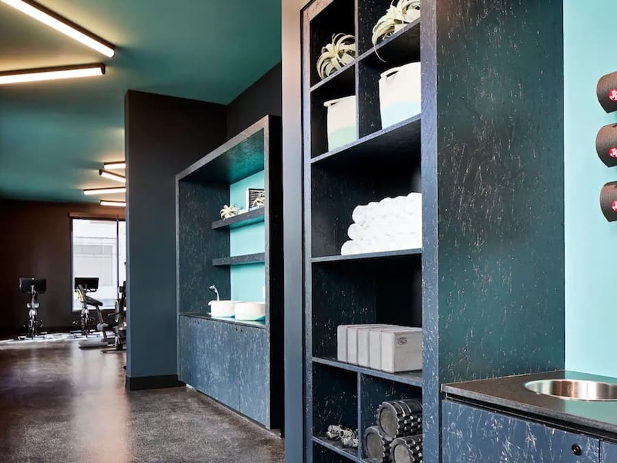 A modern bathroom with a dark teal wall, a large mirror, and shelves with toiletries.