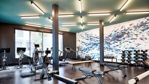A modern gym with various exercise equipment, large windows, and a unique wall mural. - El Capitan Hotel (Merced)