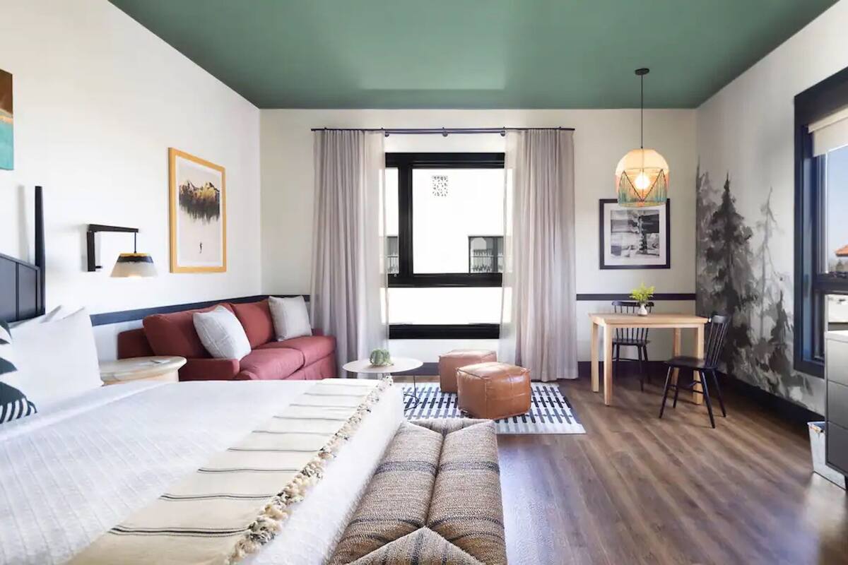 A modern hotel room with a large bed, a sofa, a dining area, and a desk.