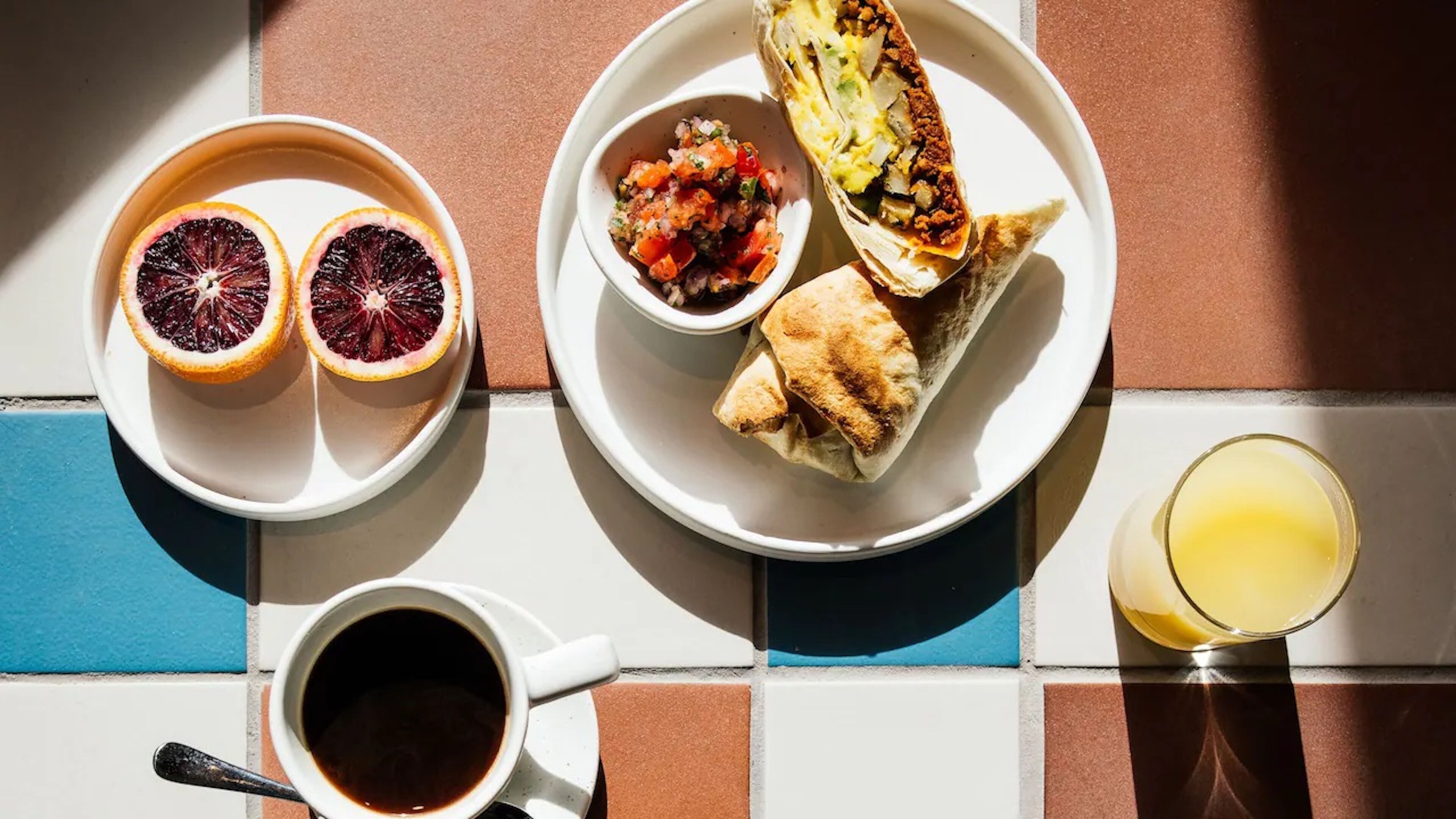 A breakfast setting with a plate of food, a bowl of salsa, two halves of a blood orange, a cup of coffee, and a glass of orange juice.