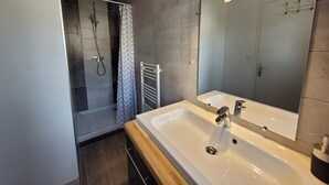 Une salle de bain moderne avec un grand miroir, un lavabo blanc et un espace douche.