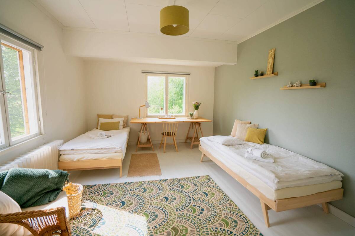 A room with two single beds, a desk with a chair, a window, and a patterned rug.
