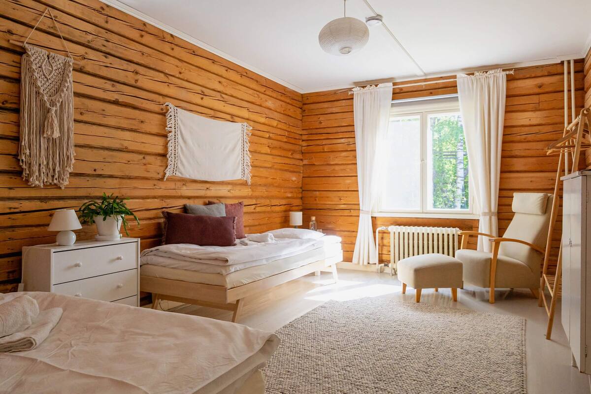 A wooden-paneled bedroom with a bed, bedside table, lamp, and a view of greenery outside.