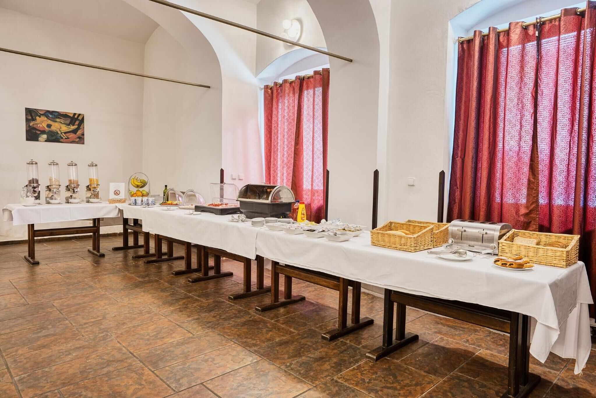 Una larga mesa de comedor dispuesta con diversos alimentos y utensilios, rodeada de paredes blancas y techos abovedados.