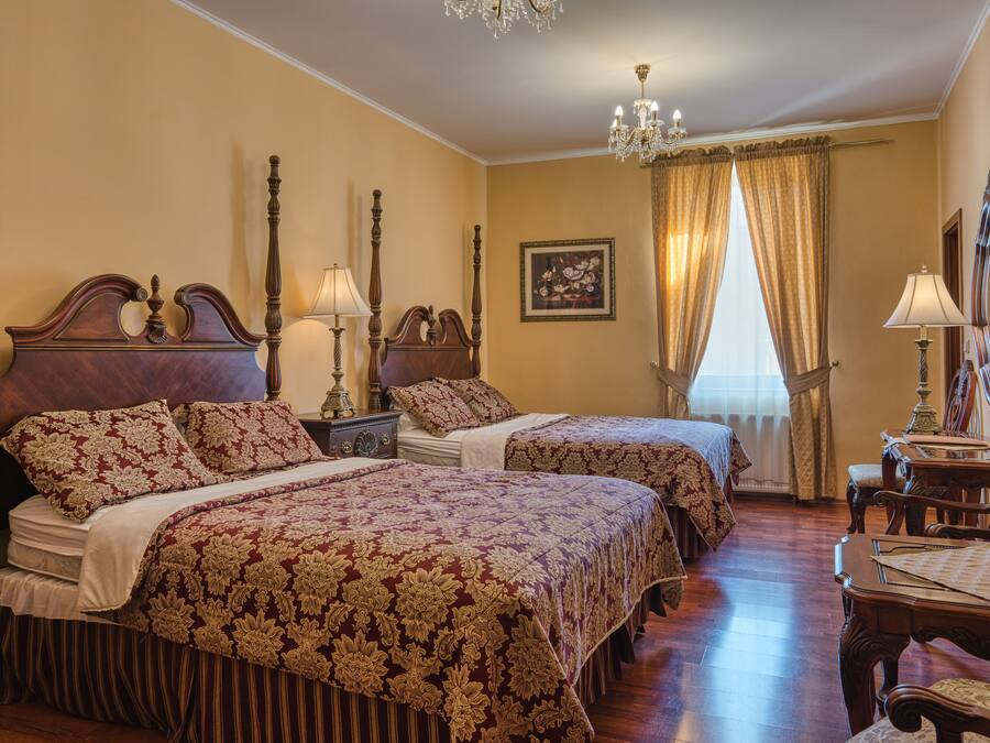 Habitación de hotel con dos camas, una araña, un cuadro y una mesa de madera.