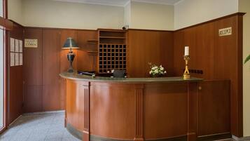 A hotel reception area with a wooden reception desk, a lamp, a flower vase, and a sign indicating the reception.