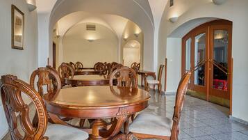 Un comedor amplio con una gran mesa redonda y sillas de madera ornamentadas, rodeado de altos techos abovedados y una escalera que conduce a otro nivel.