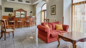Een hotel lobby met een rode bank, houten stoelen, een bar en een betegelde vloer.