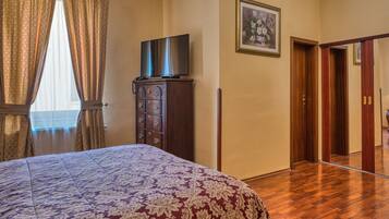 A hotel room with a large bed, a dresser, a flat-screen TV, a framed picture on the wall, and a wooden door.
