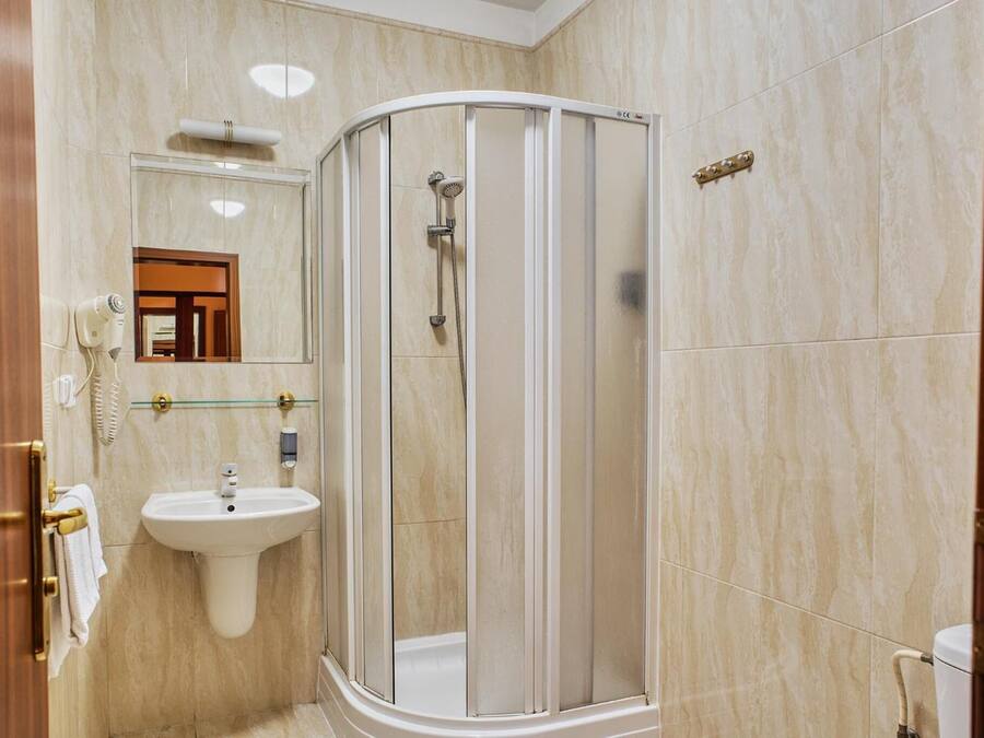 Un baño moderno con ducha de vidrio, lavamanos sobre pedestal y espejo sobre el lavamanos.