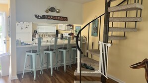 A kitchen with a bar area, a staircase with a cat tree, and a wall with a decorative sign. - "A Lil' Nauti" - 2 Bedroom Condo - Ocean Views, Emerald Isle, NC (Emerald Isle)
