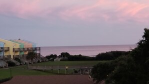A coastal view with a row of colorful buildings, a grassy area, and a bridge leading to a beach. - "A Lil' Nauti" - 2 Bedroom Condo - Ocean Views, Emerald Isle, NC (Emerald Isle)