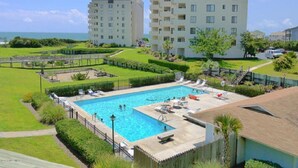A swimming pool surrounded by a well-maintained lawn and a few buildings in the background. - "A Lil' Nauti" - 2 Bedroom Condo - Ocean Views, Emerald Isle, NC (Emerald Isle)