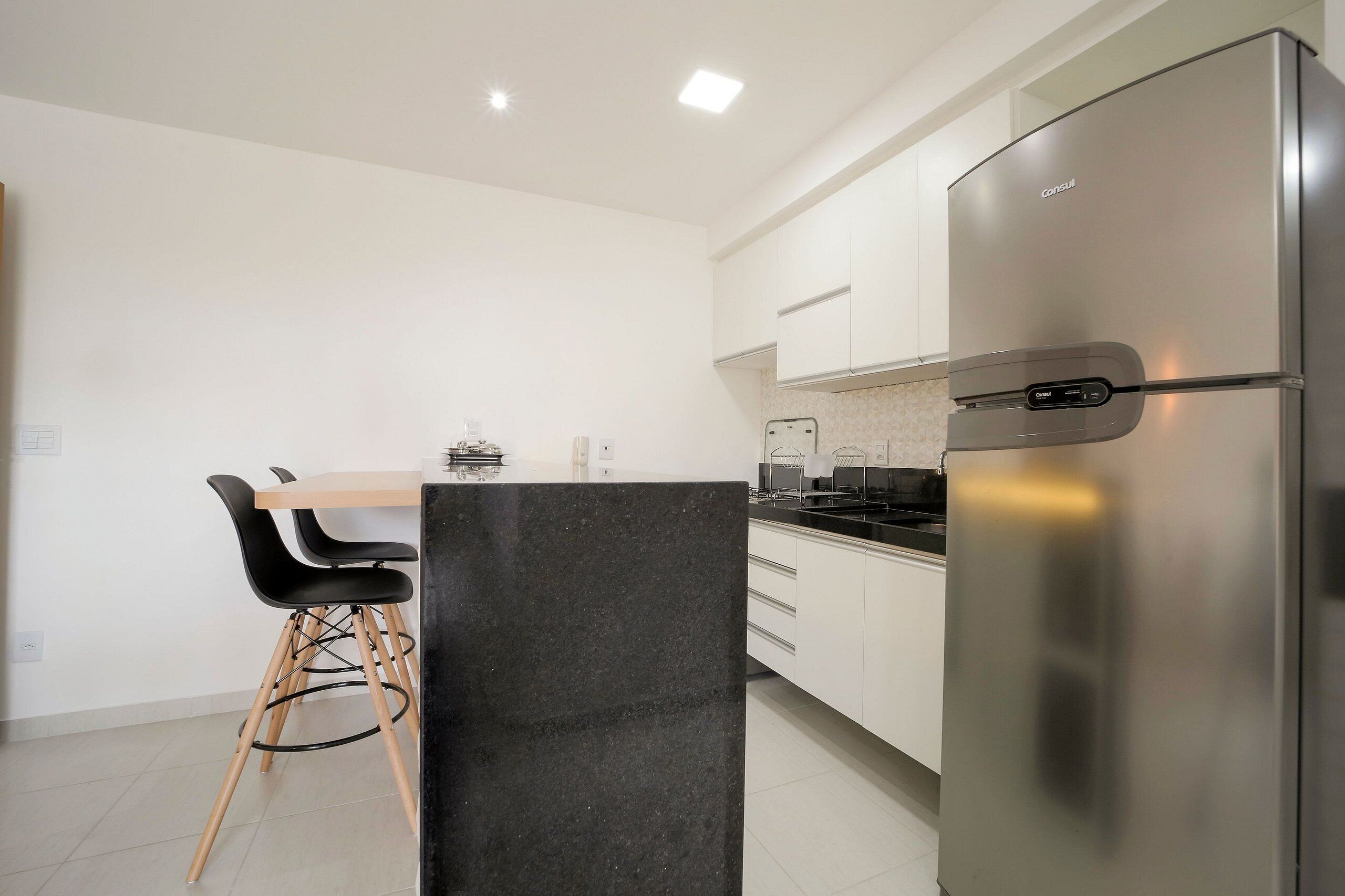 A modern kitchen with white cabinets, a stainless steel refrigerator, and a dining area with a wooden table and black chairs.