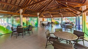 Ruime binnenruimte met hoge plafonds en een houten balkenstructuur. Er staan meerdere ronde tafels en stoelen klaar voor diners of vergaderingen.