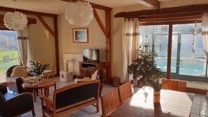 A cozy living room with a wooden ceiling, a television, a Christmas tree, and a view of a pool. - La P'tit' Fugue (La Bouexiere)