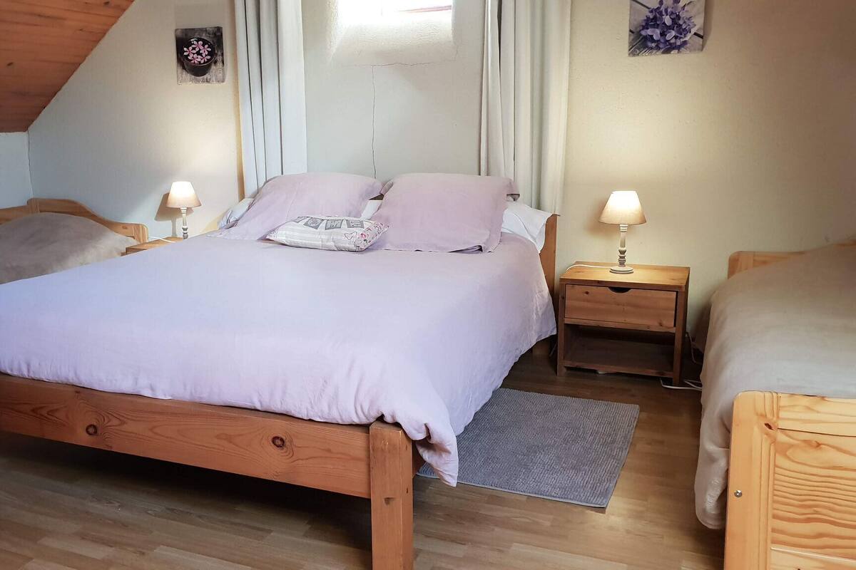 Een gezellige slaapkamer met een houten bed, twee nachtkastjes met lampen, een klein decoratie aan de muur, en een raam met gordijnen.