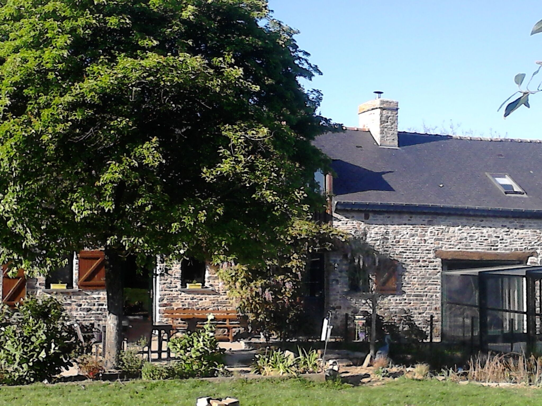 A stone building with a sloped roof, a chimney, and a wooden bench in the foreground.