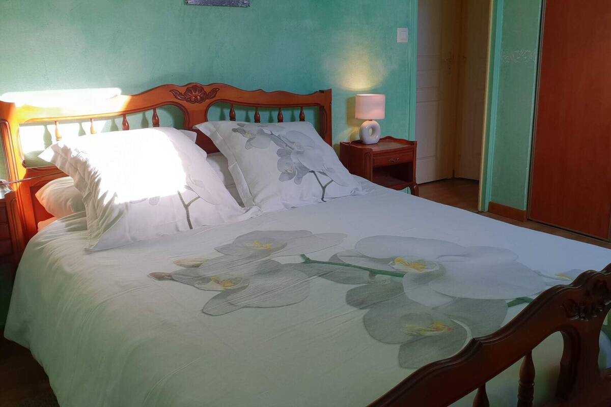 Een bed met een bloemenlaken, een nachtkastje met een lamp en een houten kledingkast.