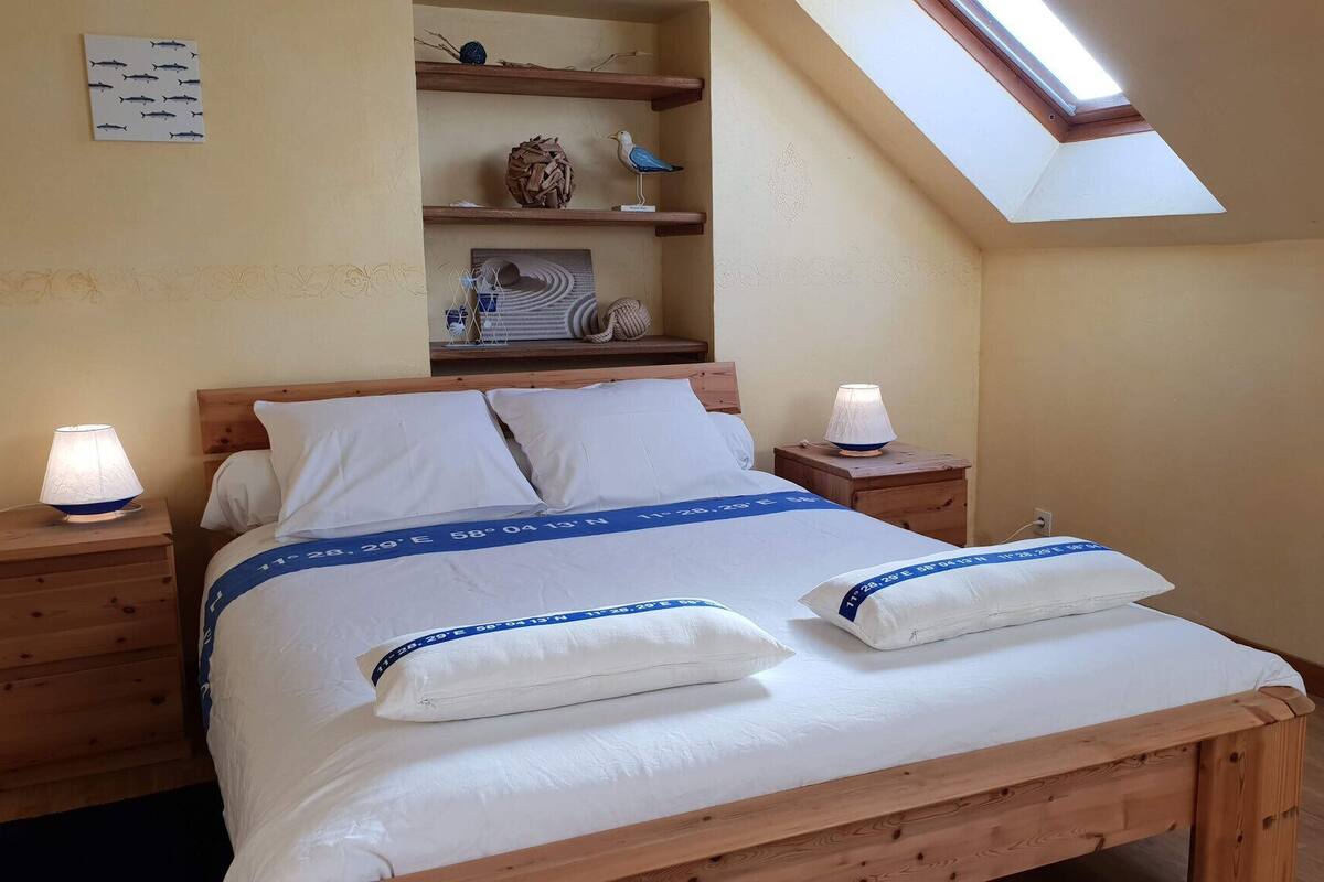 Een slaapkamer met een houten bed, twee bedlampjes, een dakraam en een plank met decoratieve objecten.
