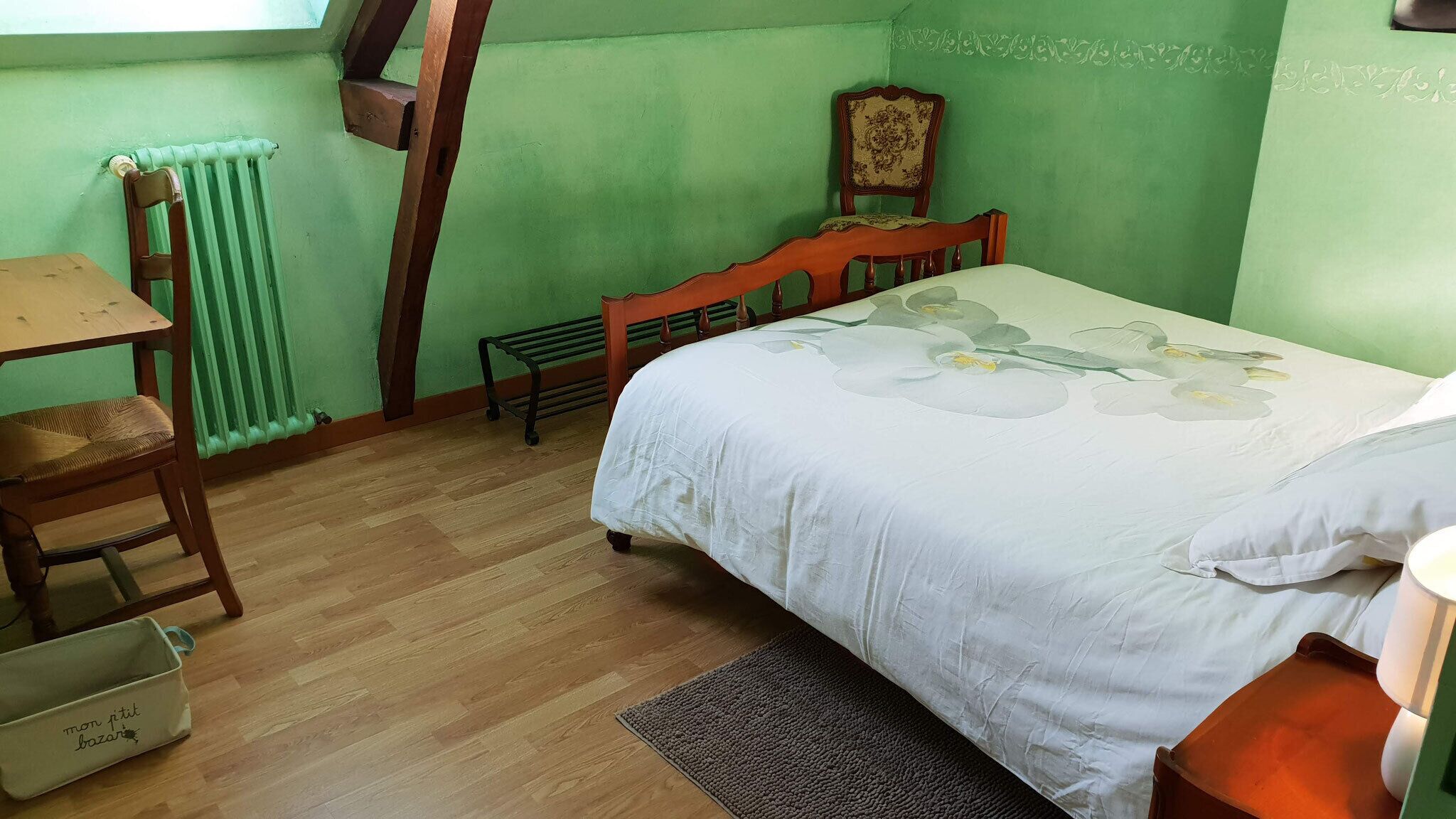 A room with a bed, a wooden chair, a small table, and a radiator.