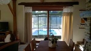 A dining area with a table and chairs, a television, and a view of an outdoor swimming pool through large glass doors. - La P'tit' Fugue (La Bouexiere)