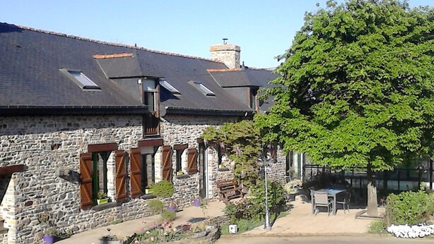A stone building with a sloped roof, multiple windows with shutters, and a small outdoor seating area. - La P'tit' Fugue (La Bouexiere)