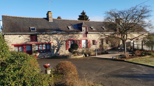 A stone building with red shutters, a chimney, and a small garden area. - La P'tit' Fugue (La Bouexiere)