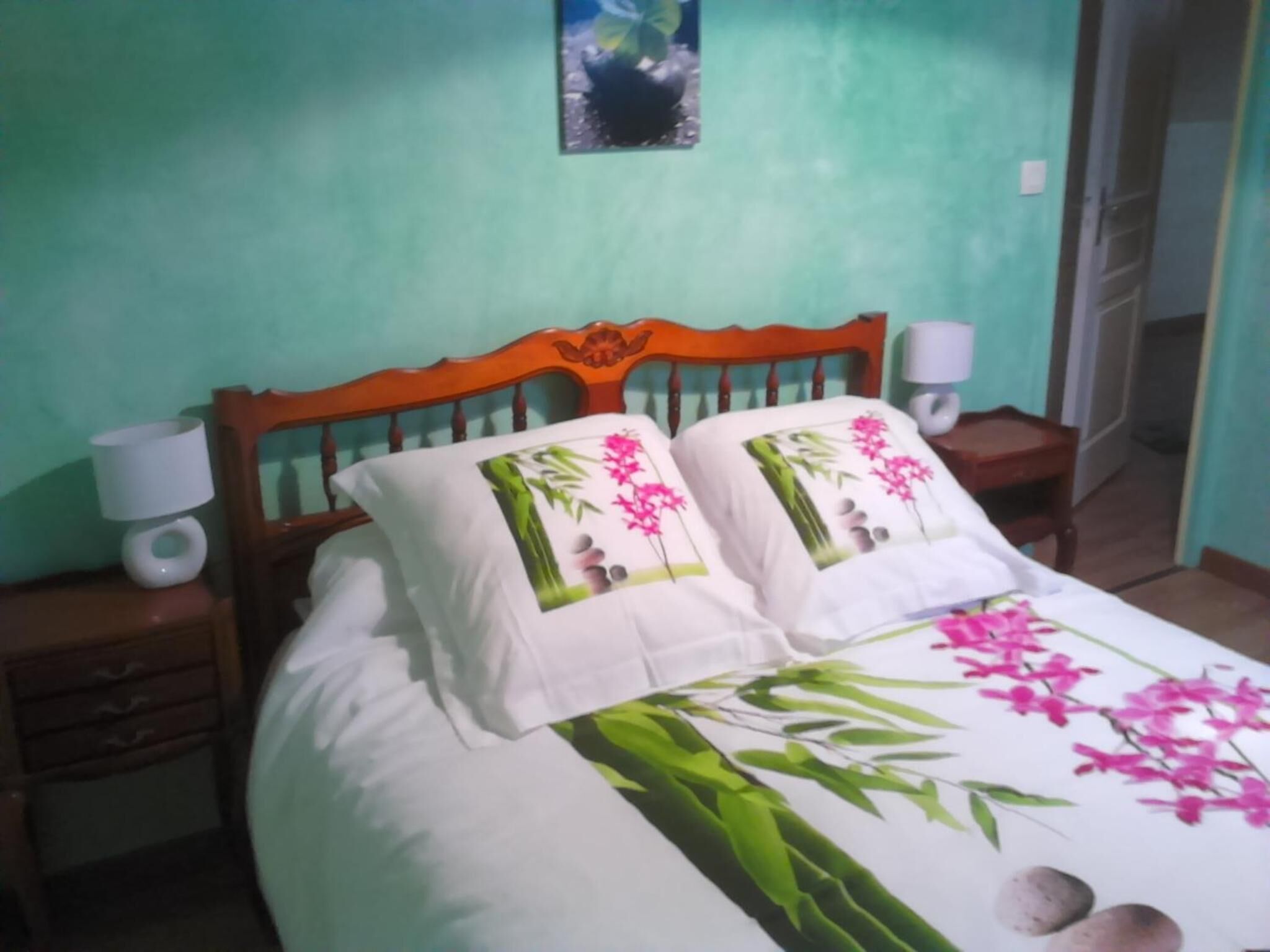 Cama com roupa de cama florida, duas luminárias de cabeceira e uma cabeceira de madeira.