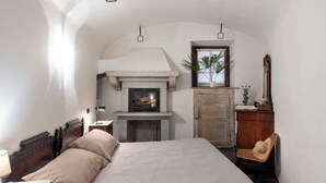 A bedroom with a stone fireplace, a bed, a wooden wardrobe, and a chair.