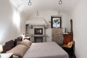 Une chambre avec une cheminée en pierre, un lit, une armoire en bois et une chaise.