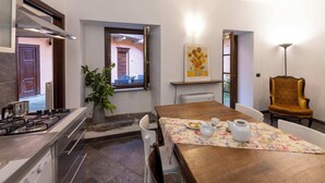 A kitchen with a stove, a dining table with chairs, a potted plant, and a painting on the wall.