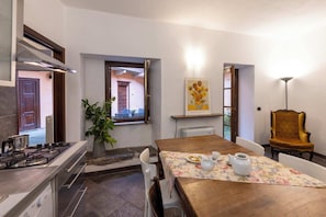 Une cuisine équipée d’une cuisinière, une table à manger avec des chaises, une plante en pot et un tableau accroché au mur.