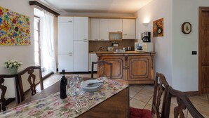Un coin repas avec une table dressée pour quatre personnes, une cuisine en arrière-plan et une porte sur la droite.