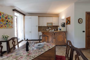 Un coin repas avec une table dressée pour quatre personnes, une cuisine en arrière-plan et une porte sur la droite.