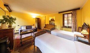 Une chambre avec deux lits, un canapé, une commode en bois, un radiateur et une fenêtre avec des rideaux.