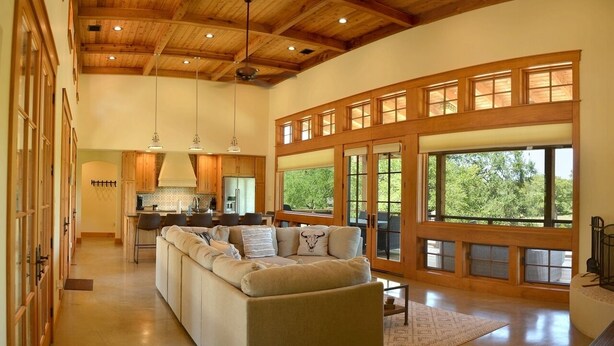 Amplia sala de estar con un sofá modular grande, vigas de techo de madera y grandes ventanales que ofrecen vistas a zonas verdes.