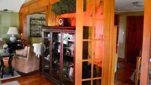 A cozy living room with a wooden ceiling, a glass-fronted cabinet, a sofa, and a lamp. - Charming cottage on the water with beautiful views (Lakeville)